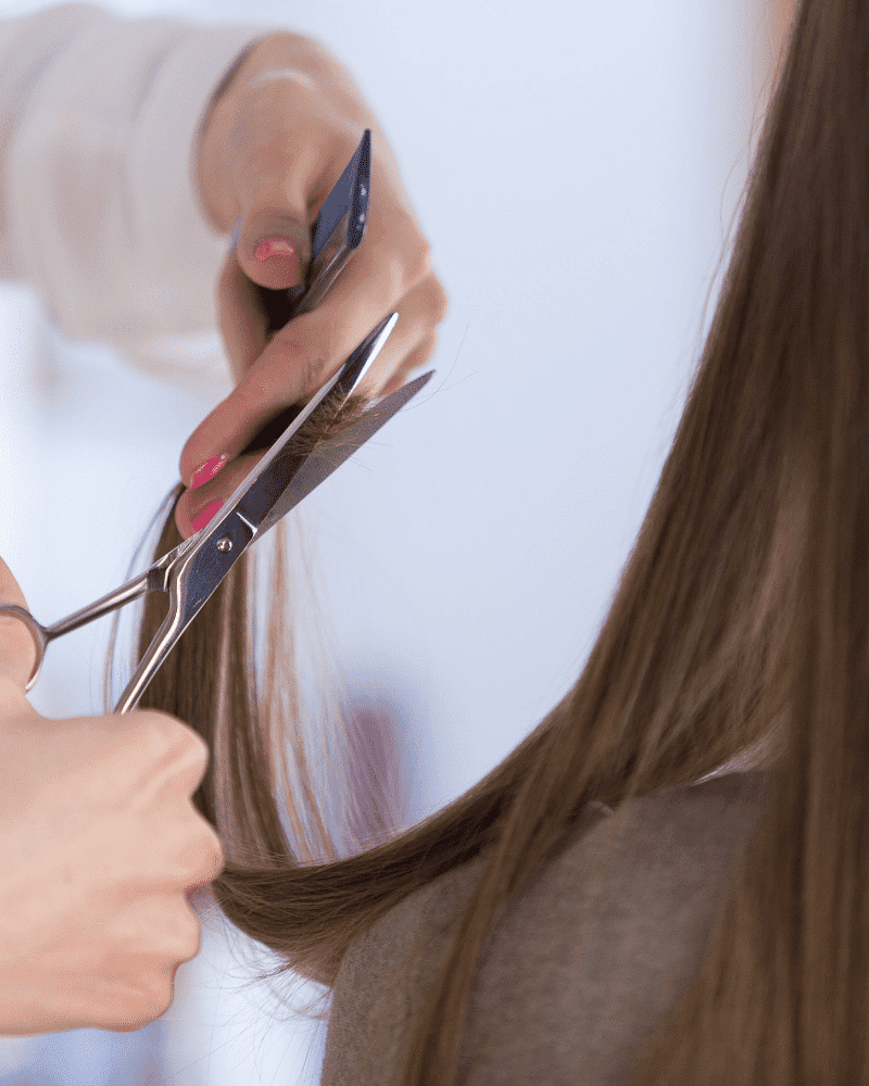 Hairdresser trimming long brown hair with scissors and comb in a salon.