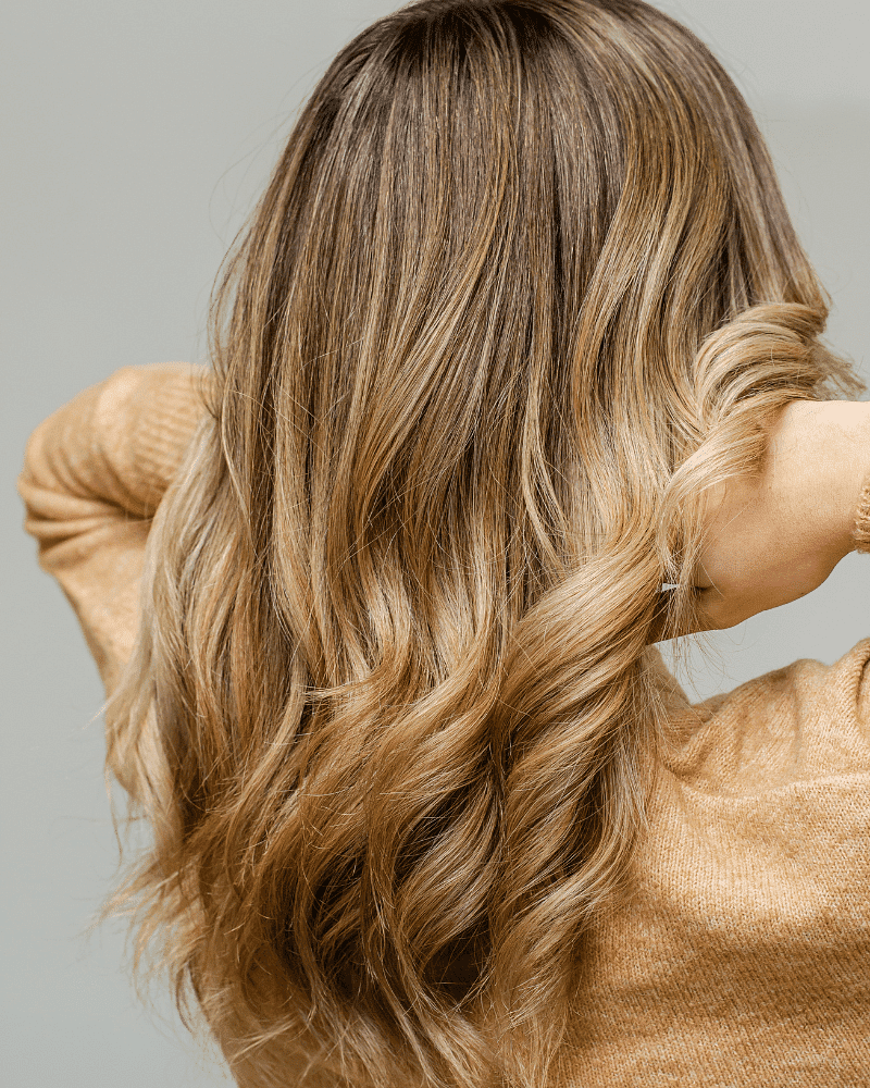 Woman with long, wavy blonde hair, showcasing her hairstyle against a neutral background.