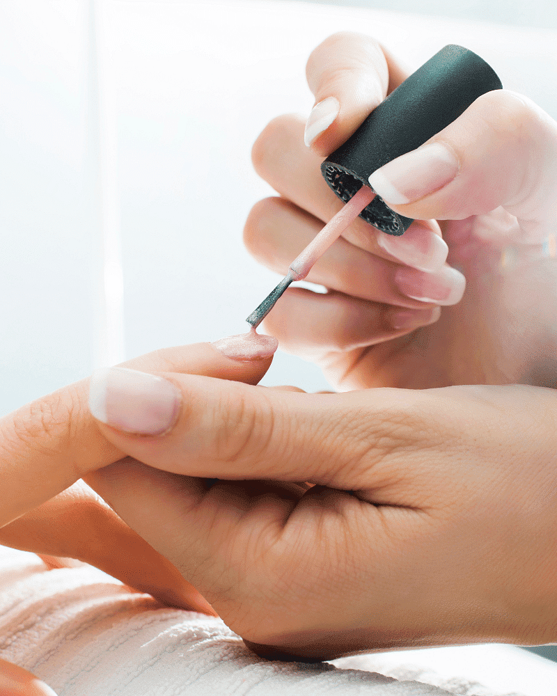 Close-up of a person applying pink nail polish to another person's nails in a beauty salon.