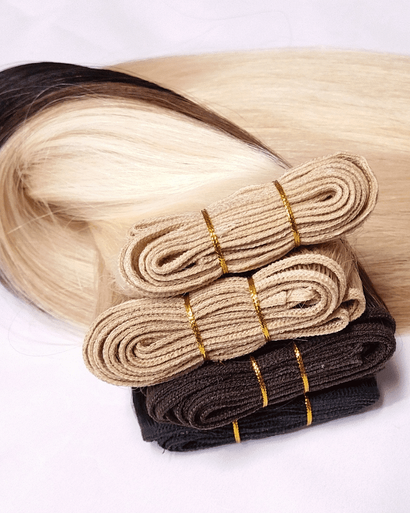 Bundles of hair extensions in different shades, neatly rolled and stacked on a white background.