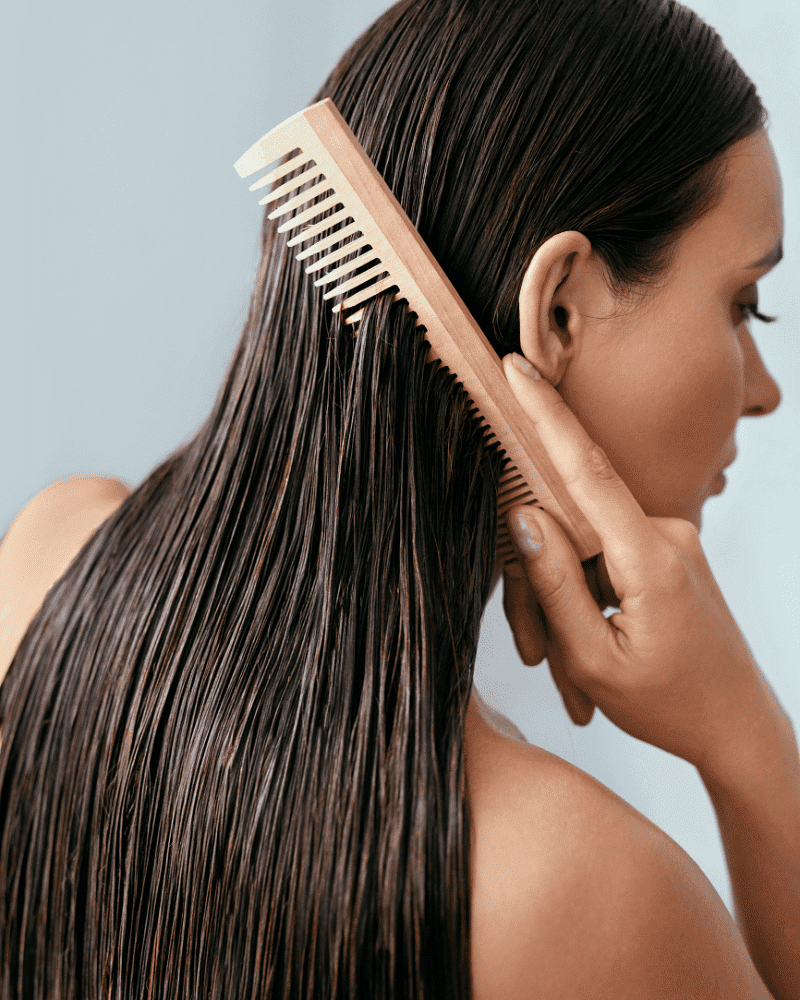 A person combing smooth, wet hair with a wooden wide-tooth comb.