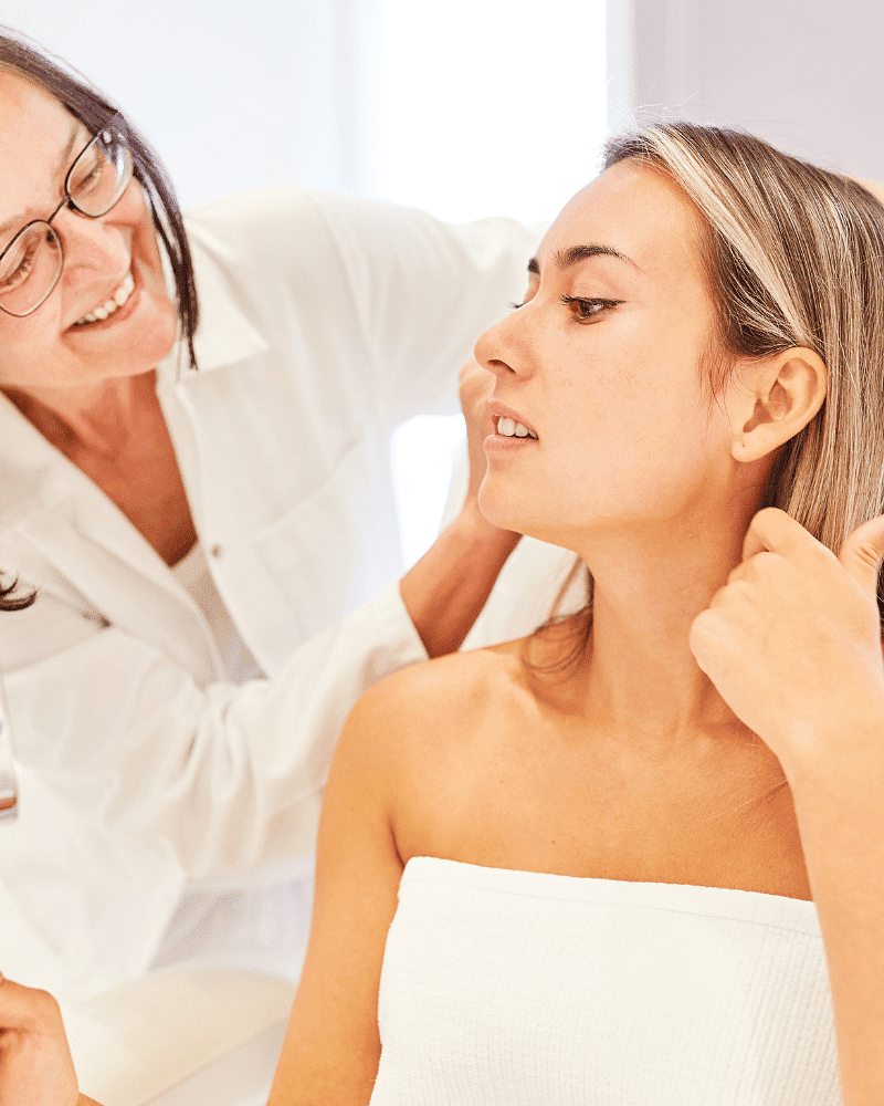 A woman getting a skincare consultation from a smiling professional in a bright room.